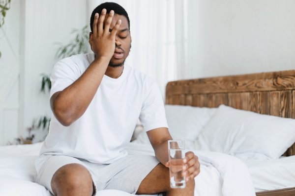Guy Having Hangover Touching Aching Head Sitting In Bed Indoors