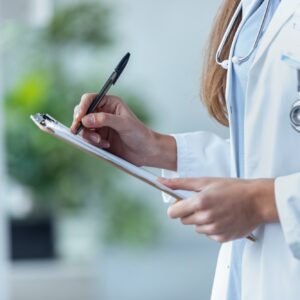 Female doctor filling up medical form at clipboard while standing in the consultation.