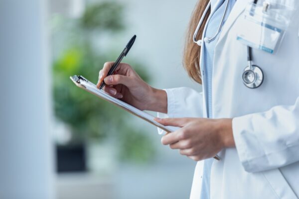 Female doctor filling up medical form at clipboard while standing in the consultation.