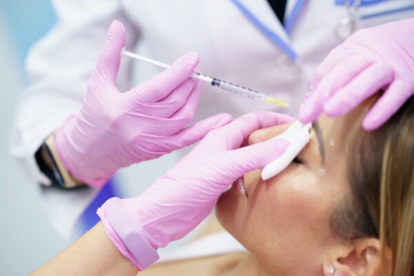 Aesthetic doctor injecting botox into the forehead of her middle-aged patient